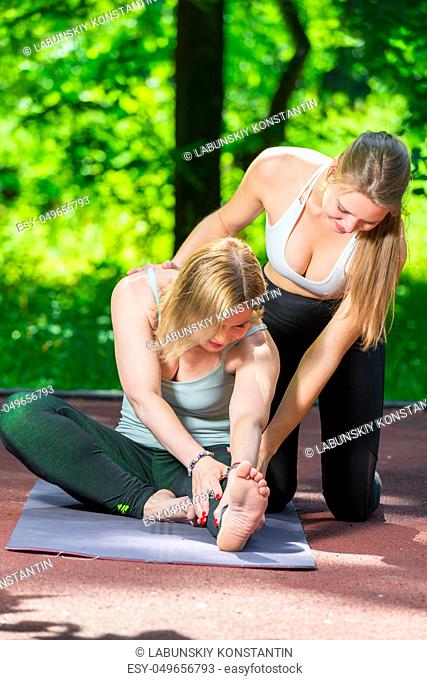 a yoga trainer helps a woman to do stretching exercises in the park