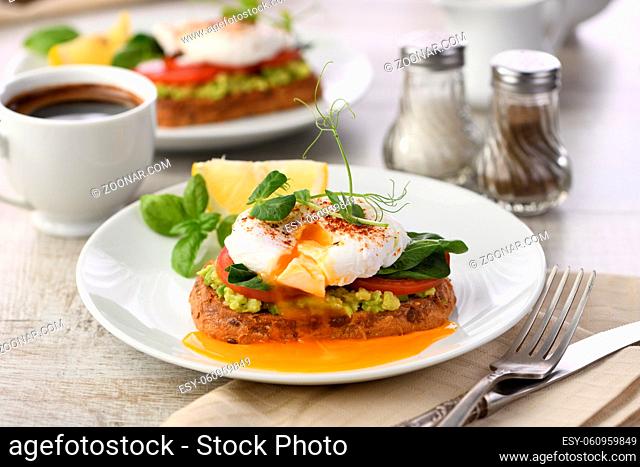 Breakfast. Best Eggs Benedict on a slice of toasted cereal bread with guacamole and spinach