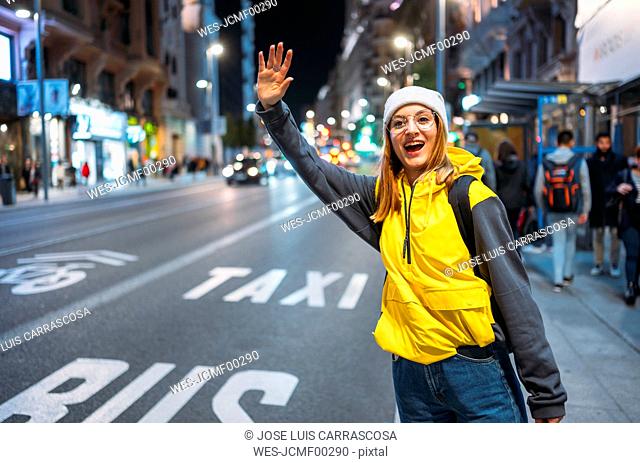 Young woman in the city hailing a taxi at night