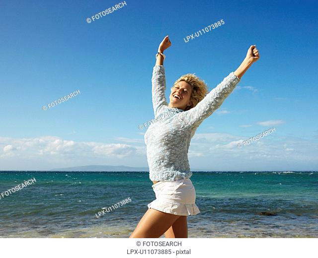 Portrait of attractive young blond woman smiling with arms raised in air on Maui, Hawaii beach