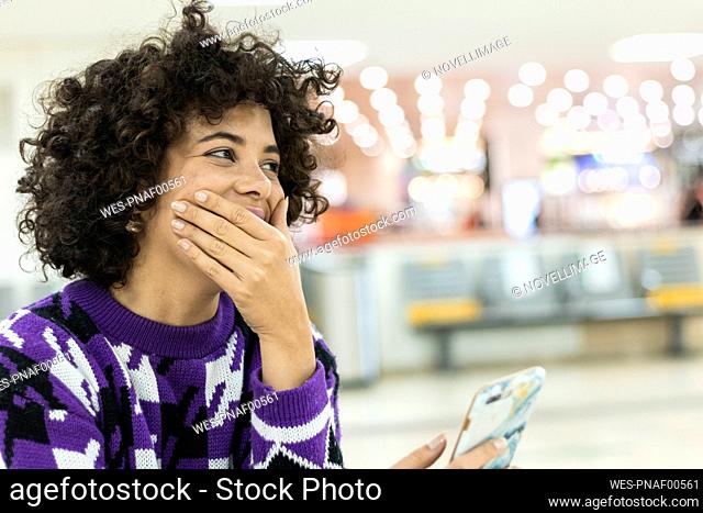 Young woman laughing while using mobile phone sitting at airport