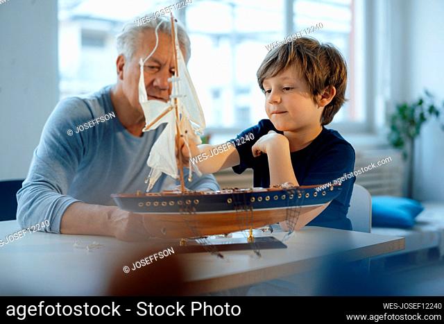 Boy and senior man looking at ship model on table