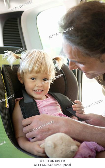 Father fastening little girl into car seat