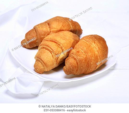 three freshly baked croissants on a white ceramic plate, a wooden white table