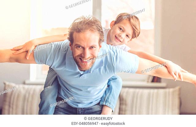 Father and son are smiling while spending time together. Little boy is sitting pickaback while imitating the flight