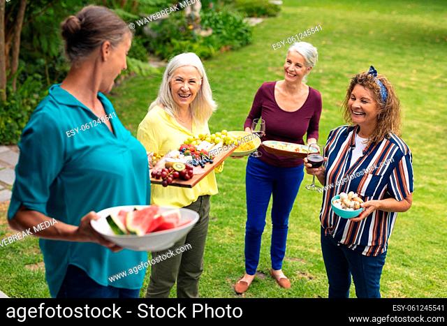 Happy caucasian senior female friends carrying food in backyard during party