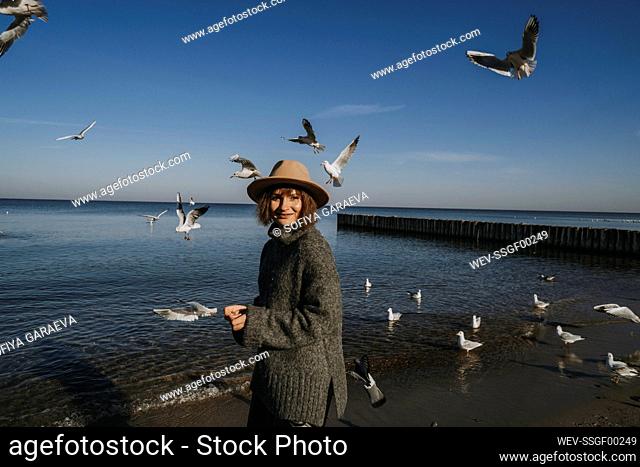 Smiling young woman feeding seagulls at sea