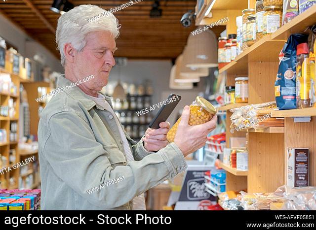 Senior man with smartphone buying groceries in a small food store