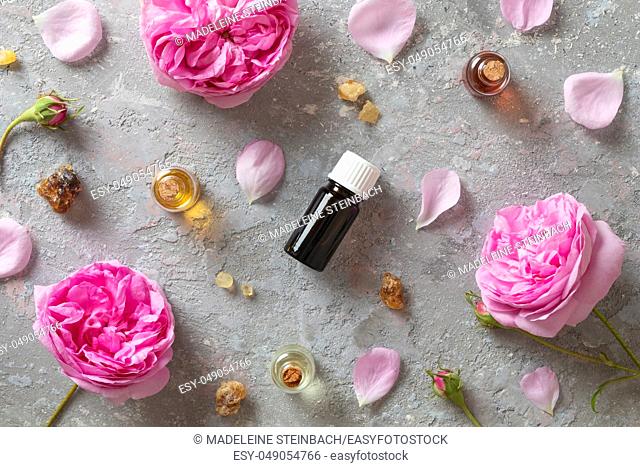 Bottles of essential oil with frankincense resin and rose de mai flowers on a grey background