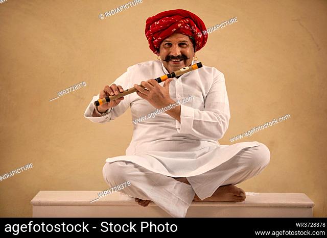 A HAPPY TURBANED MAN SITTING WITH HIS FLUTE TO PLAY
