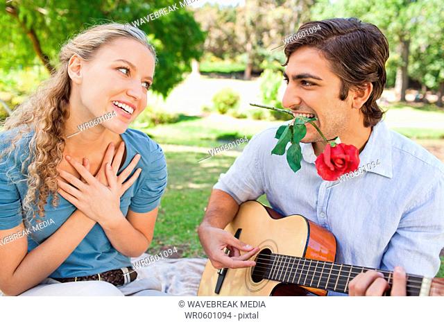 Man with a rose in his mouth playing the guitar for his girlfriend