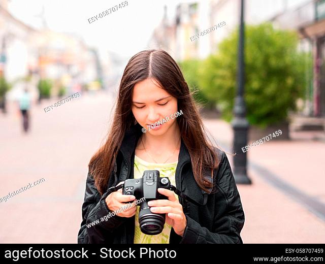 Cheerful young woman tourist watching shots in her dslr camera outdoors. Vacation photography travel concept