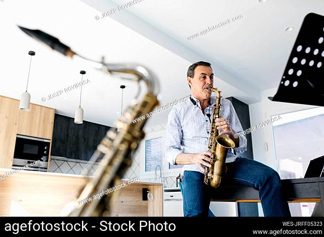 Saxophonist playing saxophone sitting on table at home