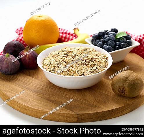 Raw oatmeal in white ceramic plate and fruits on white table, breakfast