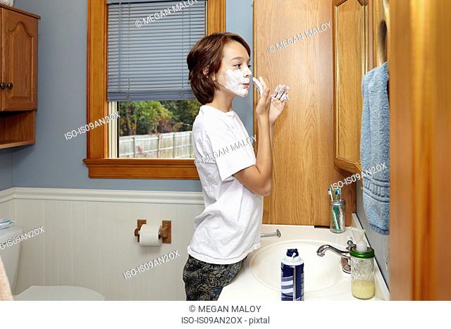 Boy applying shaving foam in bathroom mirror