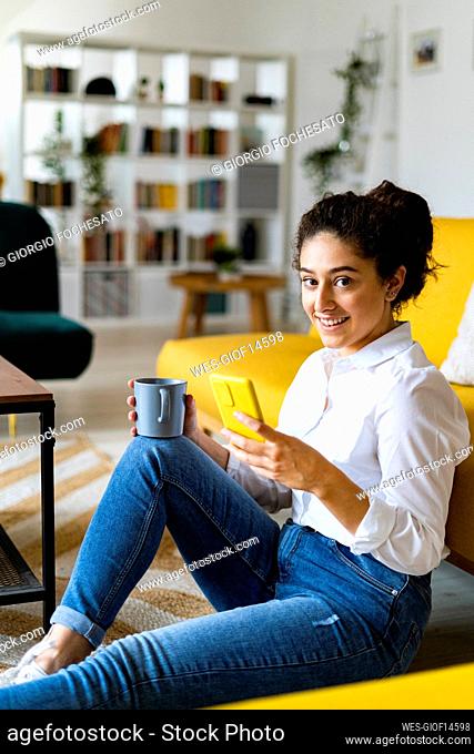 Woman with coffee mug holding smart phone at home