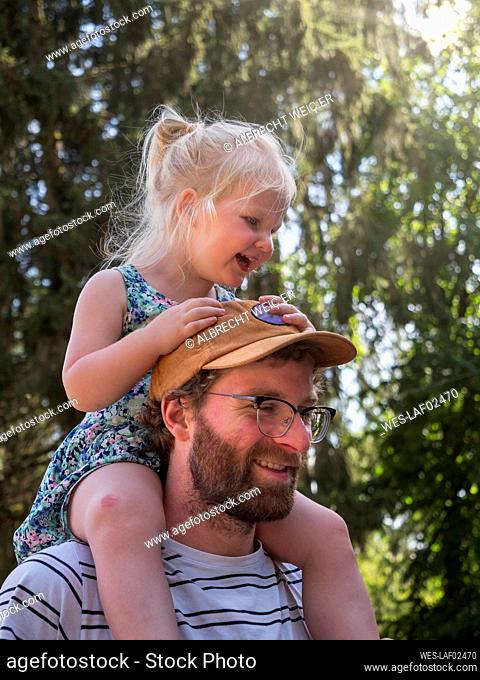 Smiling father carrying daughter on shoulder in public park