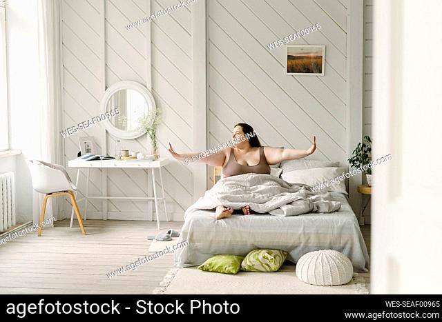Woman with arms outstretched sitting on bed at home