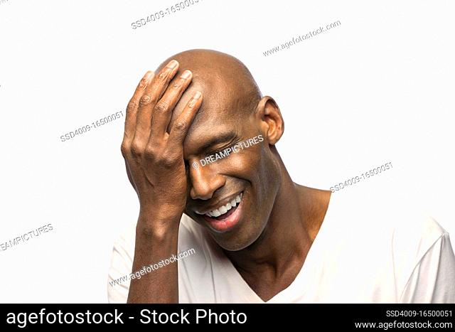 Portrait of young bald African American man with hand on his head looking down with eyes closed