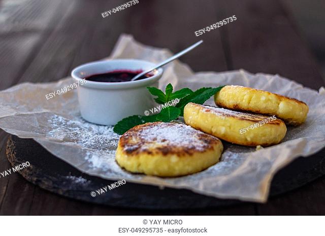 Fried cheesecakes or pancakes on craft paper on stone plate with blueberry jam