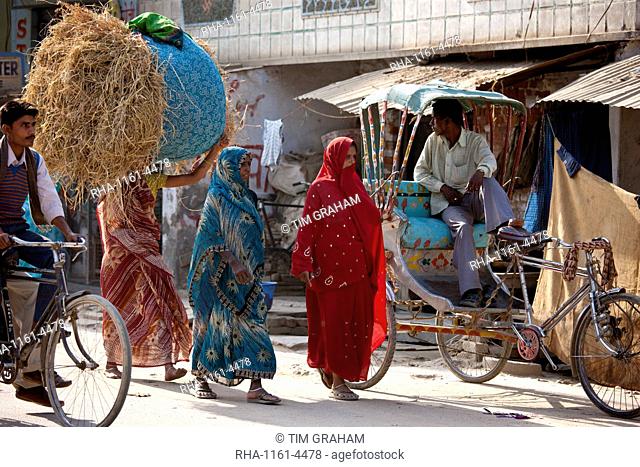 Indian women walking in the street, one carrying straw bale on head, in Nandi near Varanasi, Benares, Northern India