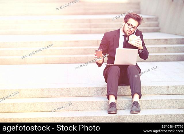 Toned picture of businessman speaking on mobile or smart phone while sitting on stair in city centre and working on laptop computer