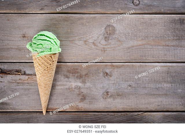 Top view single scoop green tea ice cream in a waffle cone over old rustic wooden background with copy space