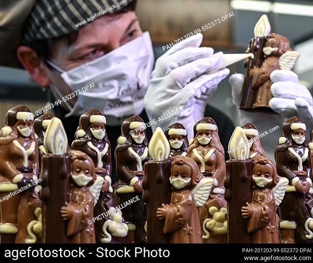 02 December 2020, Brandenburg, Hornow: Anne Walter, chocolatier from the Confiserie Felicitas, decorates small Christmas figures with a mouth and nose protector...