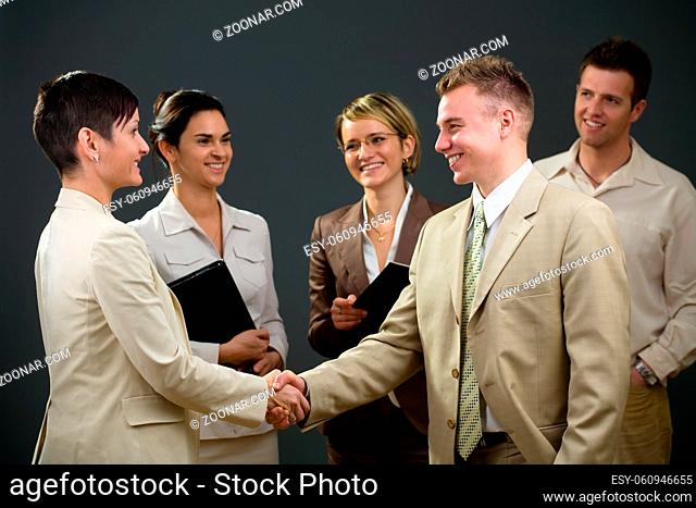 Businessman and businesswoman shaking hands in front of smiling colleagues