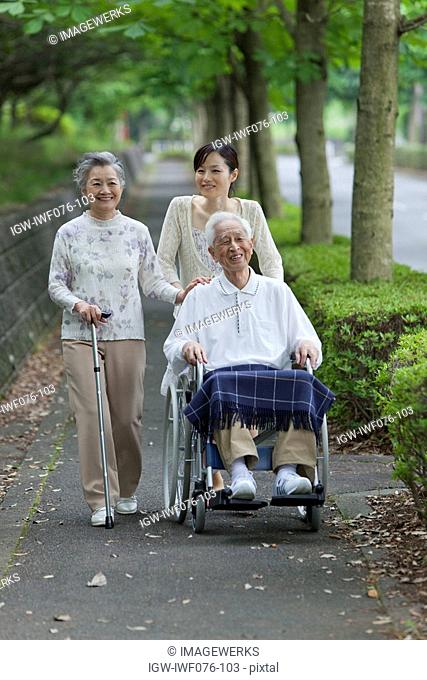 Japan, Tokyo Prefecture, Woman pushing senior man in wheelchair through footpath, smiling