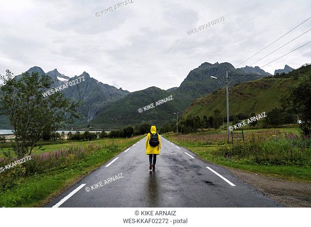 Norway, Lapland, Vesteralen Islands, Young man walking on empty road, rear view