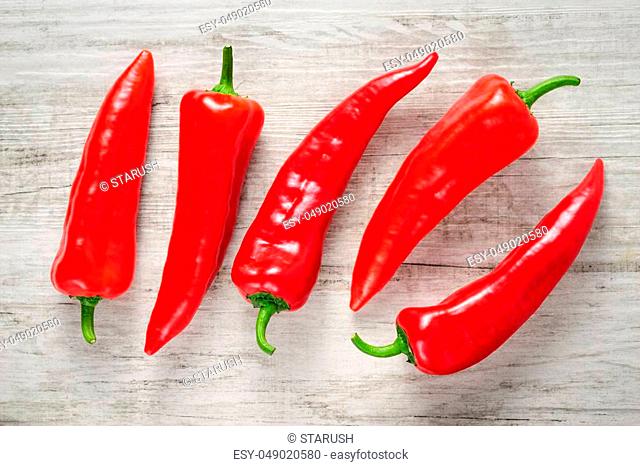 Five ripe sweet red Kapia peppers on white wood background