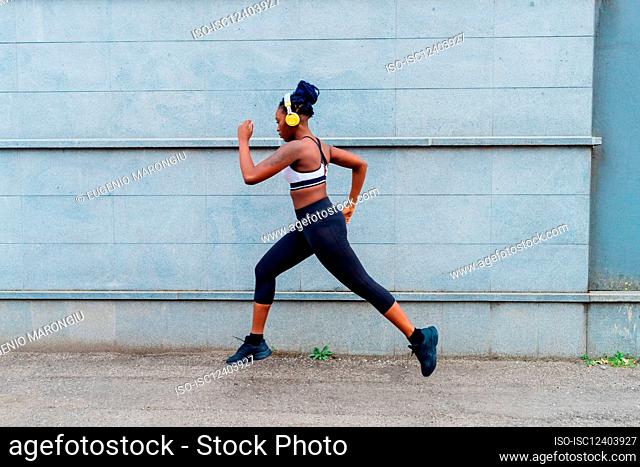 Italy, Milan, Woman in sports clothing and headphones jogging in city
