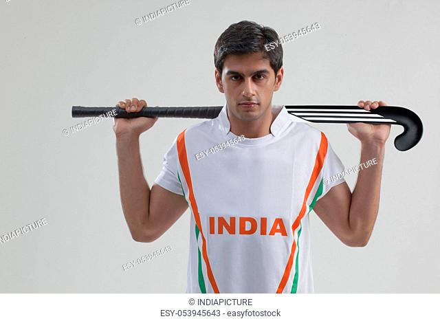 Portrait of confident young man with hockey stick isolated over gray background