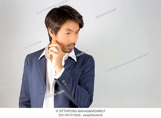 Portrait Man in Navy Blue Suit Looking Below and Touch Chin Pose. Portrait man in navy blue suit and white shirt on left frame of grey background in smart style