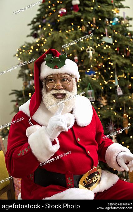 African American Santa Claus sitting in front of illuminated Christmas tree