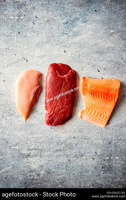Three pieces of different kinds of raw meat. Chicken brest, beef steak and salmon fillet. Top view on gray stone background