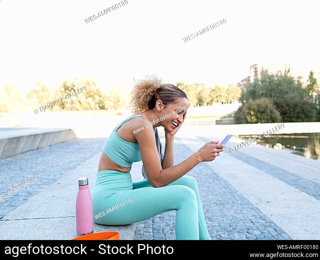 Happy sportswoman using smart phone on steps