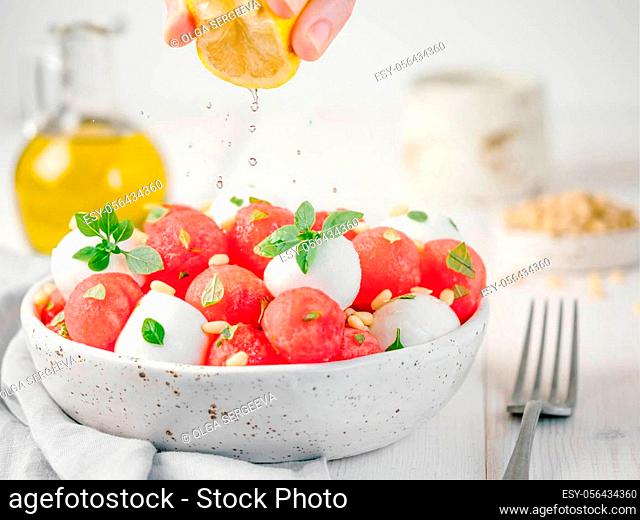 Ideas and recipes for healthy summer lunch food - watermelon caprese salad with mozzarella and basil. Watermelon balls and mini mozzarella balls on white wooden...