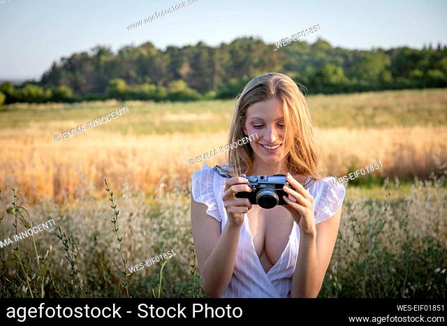 Smiling young woman looking at camera while standing in field