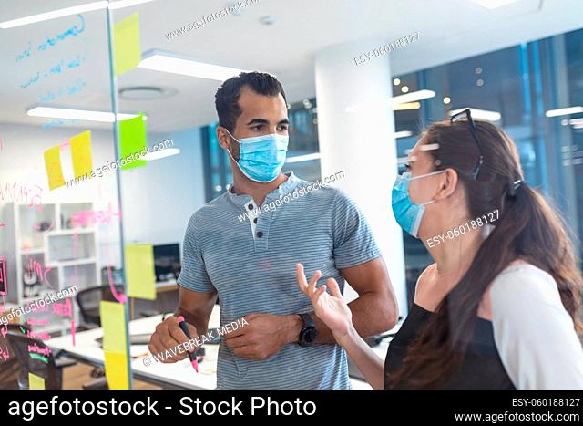 Two diverse creative colleagues wearing face masks talking at meeting