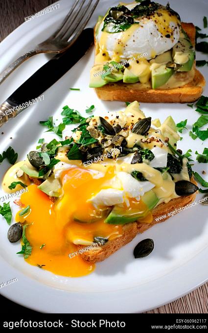 Eggs Benedict on toast with Dutch sauce, slices of avocado