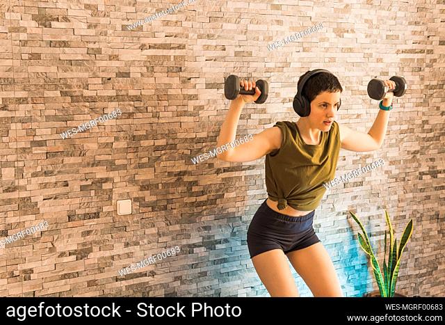 Woman doing exercise with dumbbells in front of wall