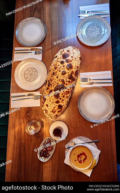 23 March 2023, Hamburg: A glass of water, a glass of tea, a bowl of dates, soup and Sisme Ekmek stone-baked bread are on the table at the Pamukkale Köz...