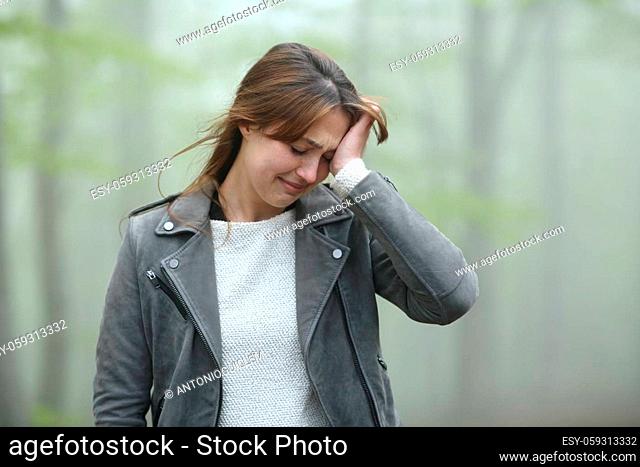 Sad woman complaining alone walking in a foggy forest