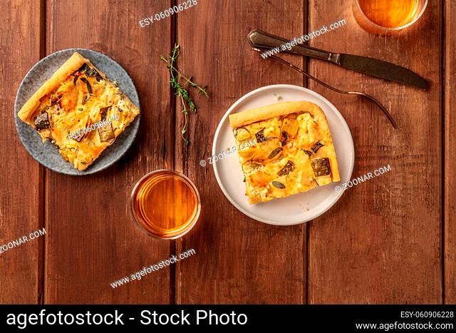 Slices of a zucchini and goat cheese pie with thyme, shot from above on a dark rustic wooden background with white wine