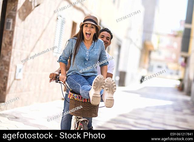Joyful couple riding bicycle outdoors in city. Man with delighted woman sitting on handlebar while riding bicycle in city