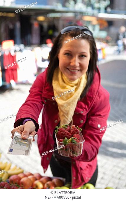 Young woman paying for basket of strawberries
