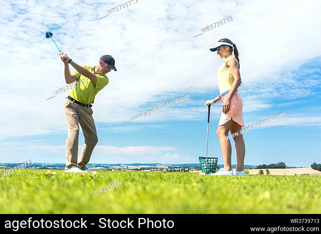 Full length of a young woman smiling while practicing the correct move for striking during golf class with a skilled professional player outdoors