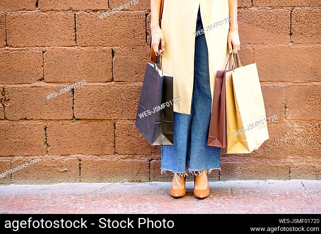 Woman carrying shopping bag while standing against brick wall